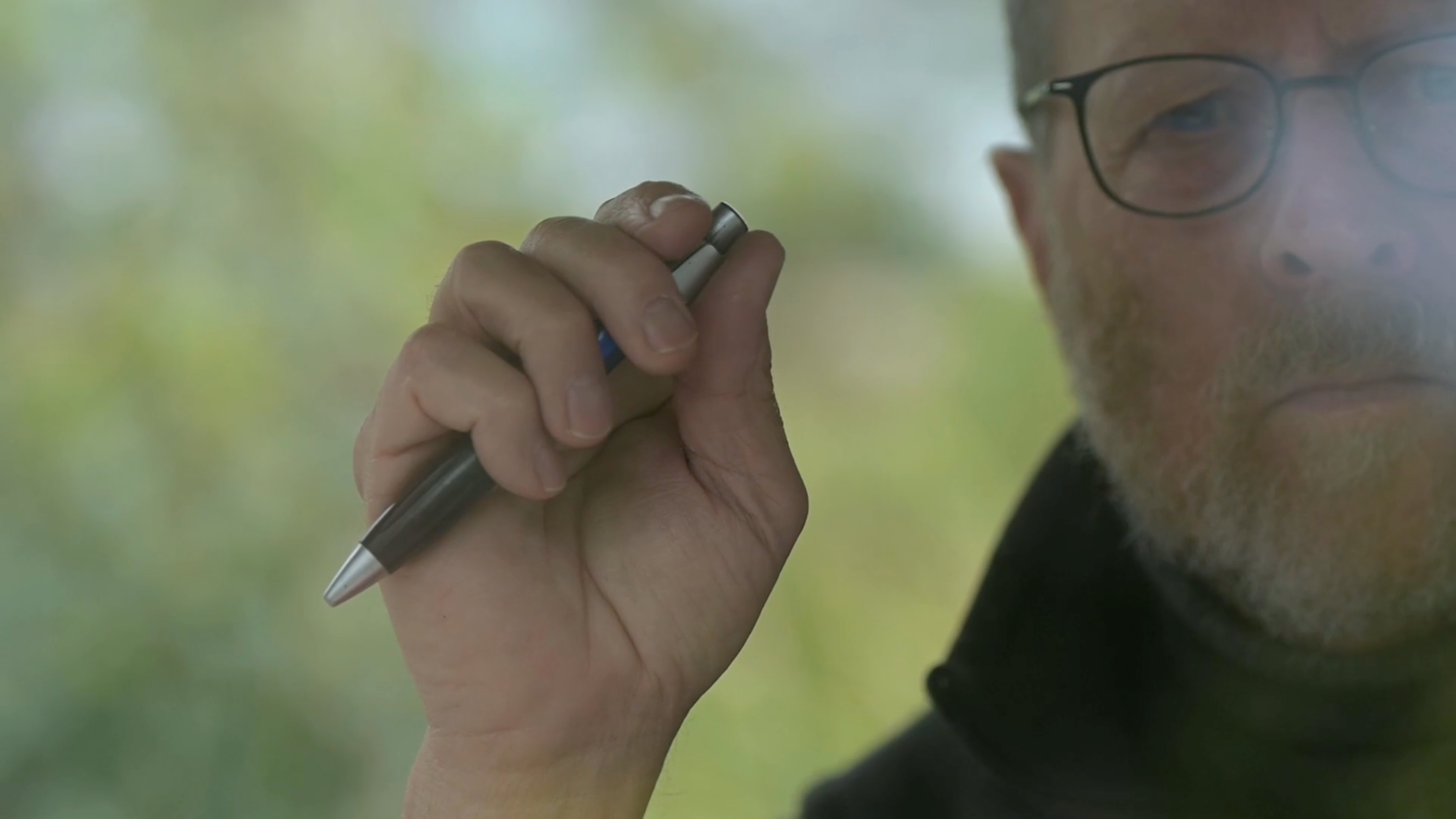 poet looks at camera, holds pen in right hand, poised in the air